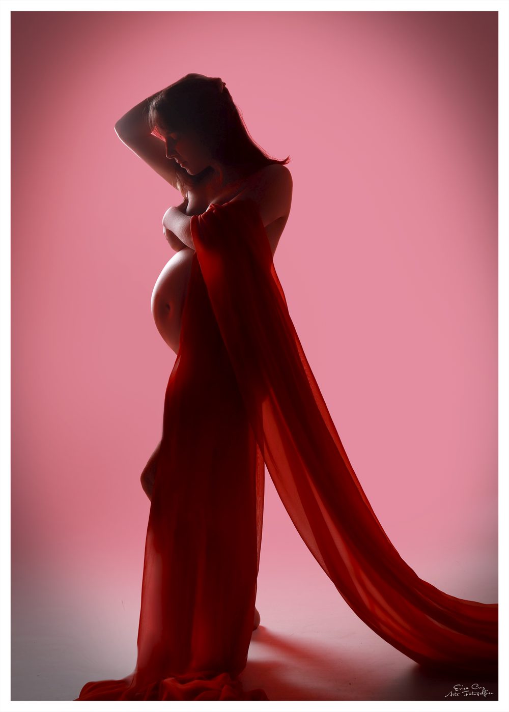 Silueta de futura mamá envuelta en tela roja con fondo rosado, sesión de embarazo Erica Cruz
